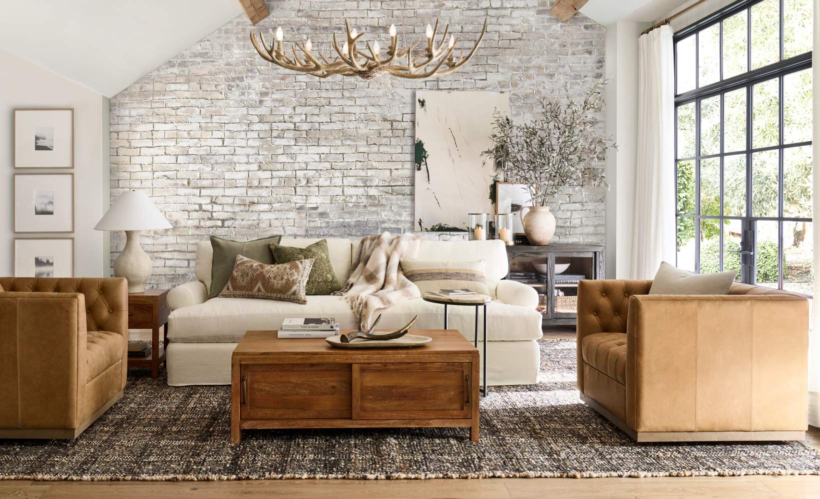 Stylish living room blending rustic and modern design elements. The space features a white sofa with neutral throw pillows, two tan tufted armchairs, and a wooden coffee table.