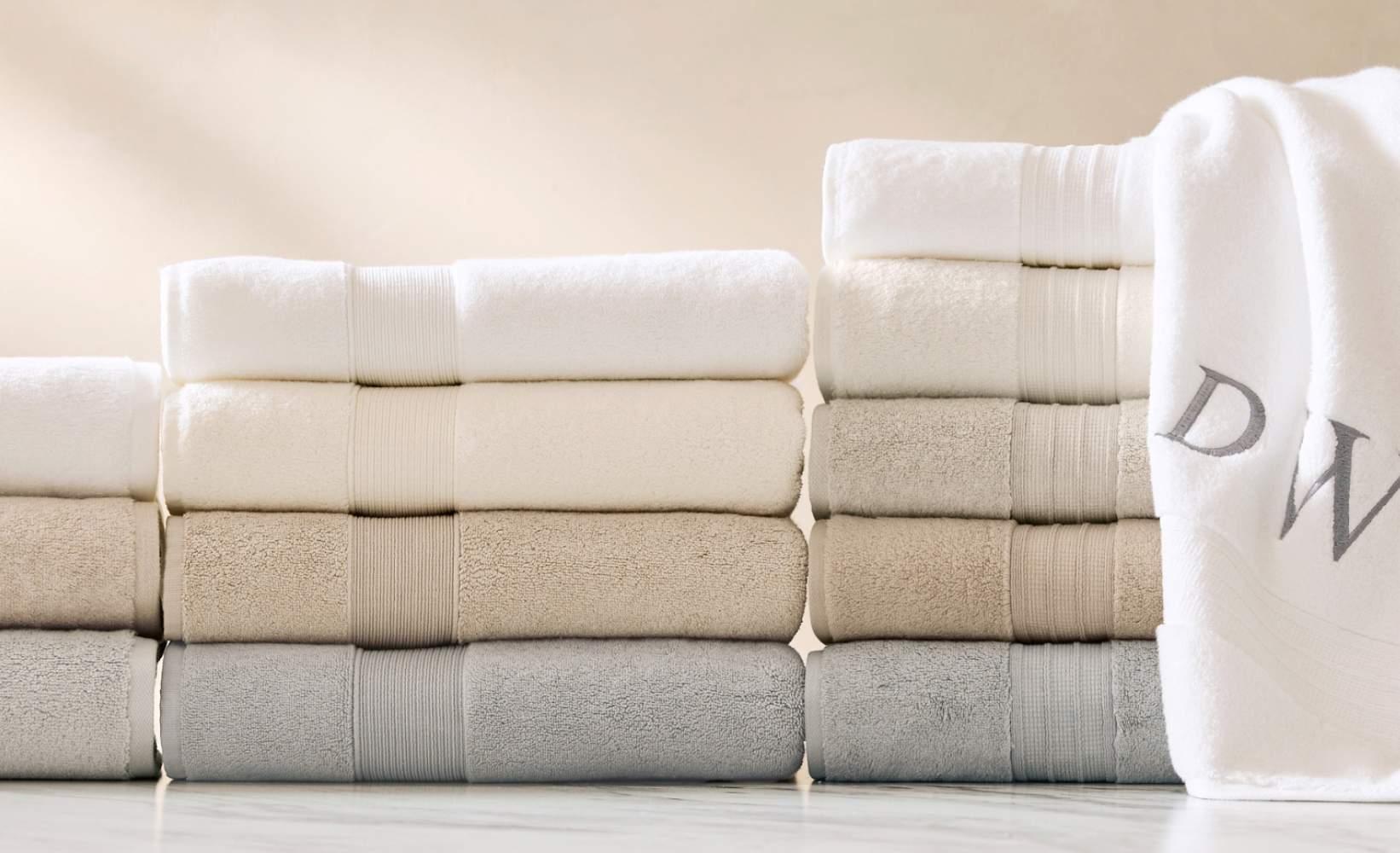 Luxury hotel-quality bath towels stacked in neutral colors - white, ivory, beige, and gray - with monogrammed detail, showcasing high-end bathroom linens with elegant ribbed texture Luxury hotel-quality bath towels stacked in neutral colors - white, ivory, beige, and gray - with monogrammed detail, showcasing high-end bathroom linens with elegant ribbed texture