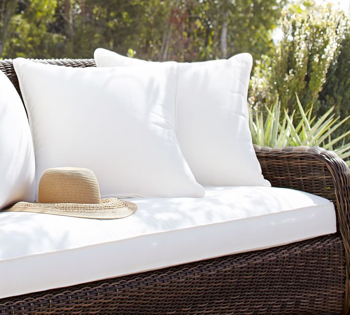 White cushioned outdoor sofa with brown wicker frame and a straw hat resting on the seat