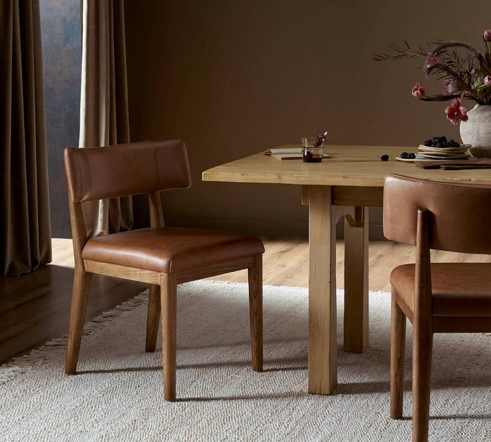 A wooden dining table with brown leather upholstered chairs around it in a warmly lit room.