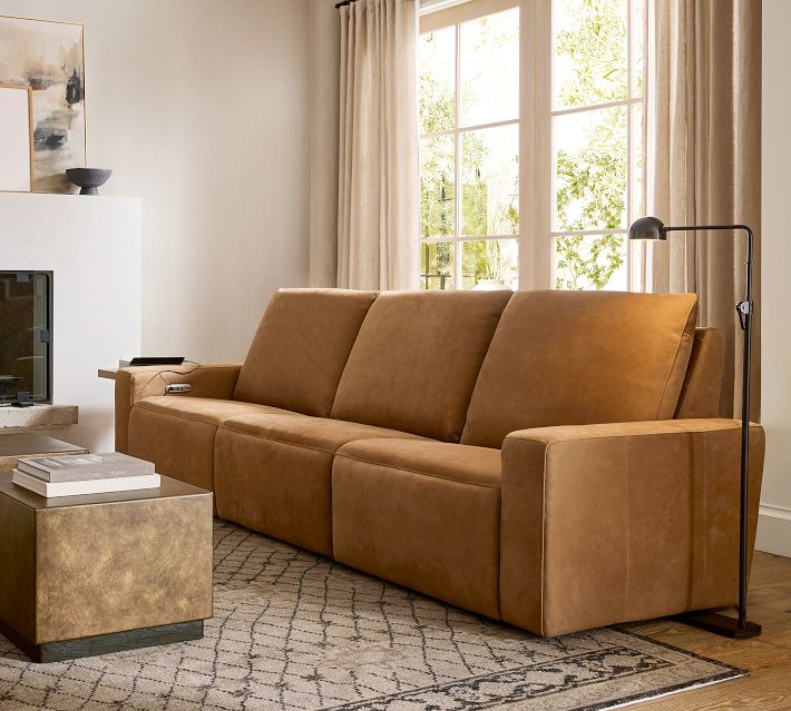 Three-seat tan leather sofa with blankets and lamp in living room setting.