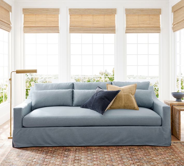 Light blue couch with two throw pillows in bright room with large windows.