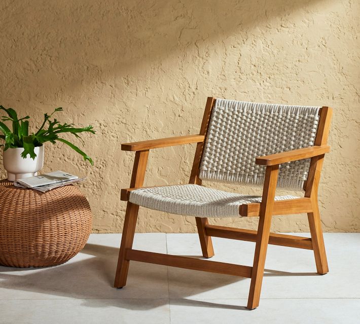Outdoor lounge chair with woven rope seat and backrest, wooden frame in light brown, set on tiled floor next to a woven ottoman with plant