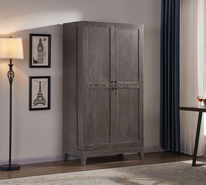 A grey wooden wardrobe cabinet in a living room with decorative pictures and a lamp nearby.