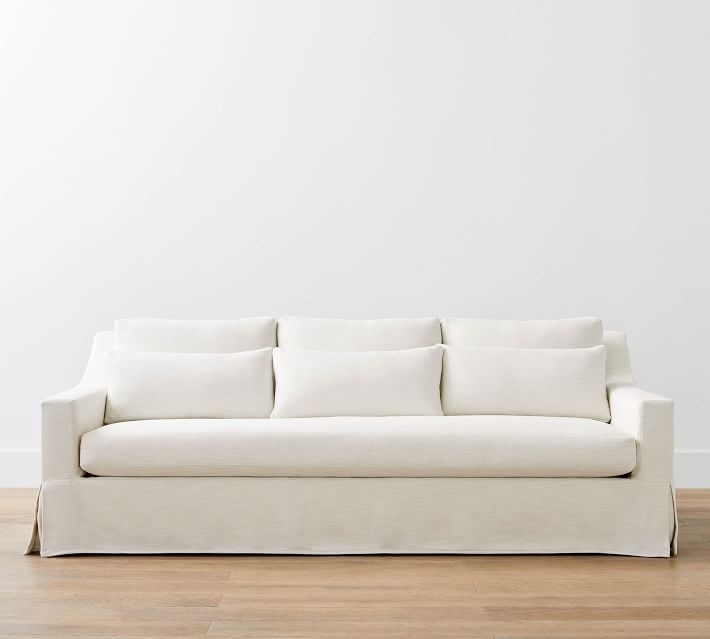 Cream-colored sofa with skirted base and three back cushions, placed on wooden floor.