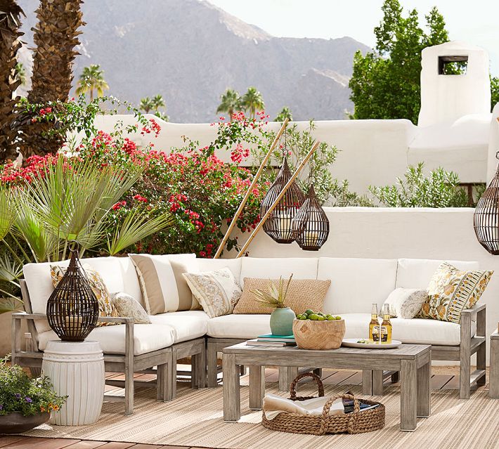 Corner seating area on patio with white cushions and greenery, decorative lanterns