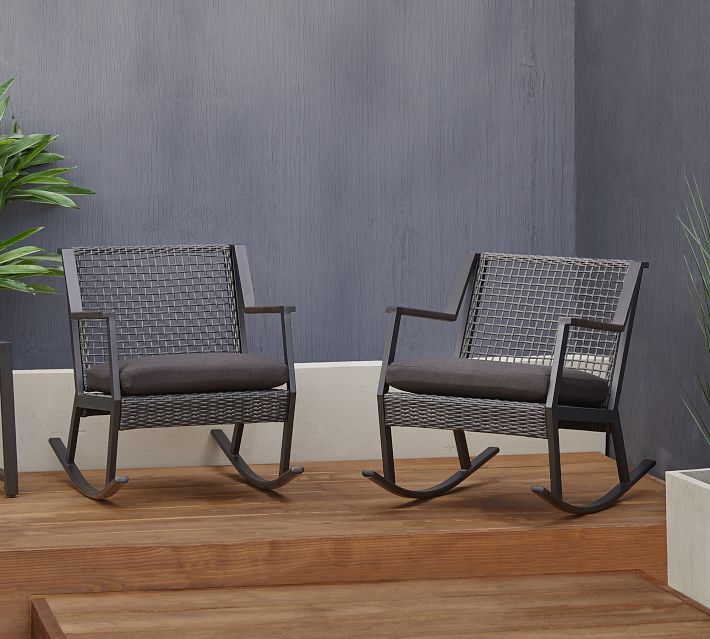 Two wicker outdoor rocking chairs on a wooden deck with railing and plants