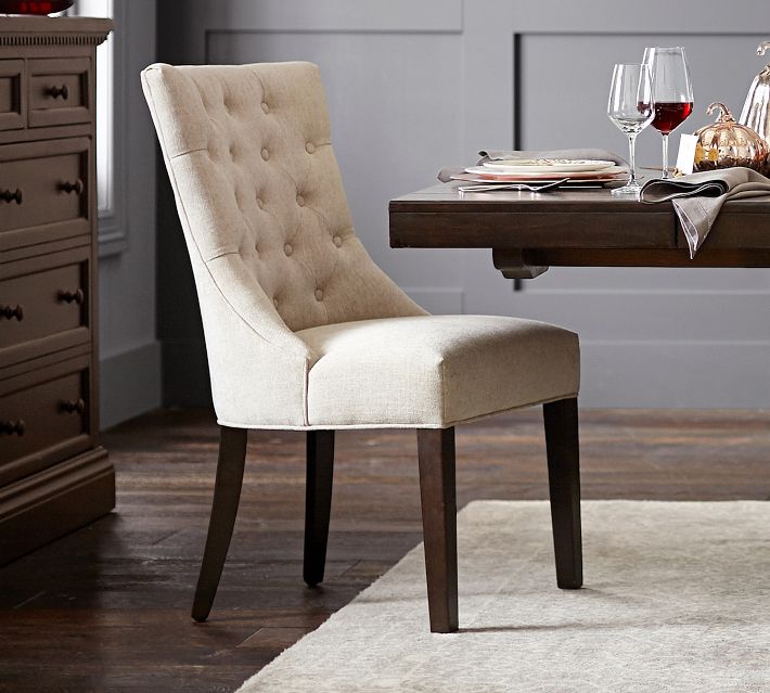 Cream upholstered dining chair with button-tufted back and dark wooden legs beside a dining table