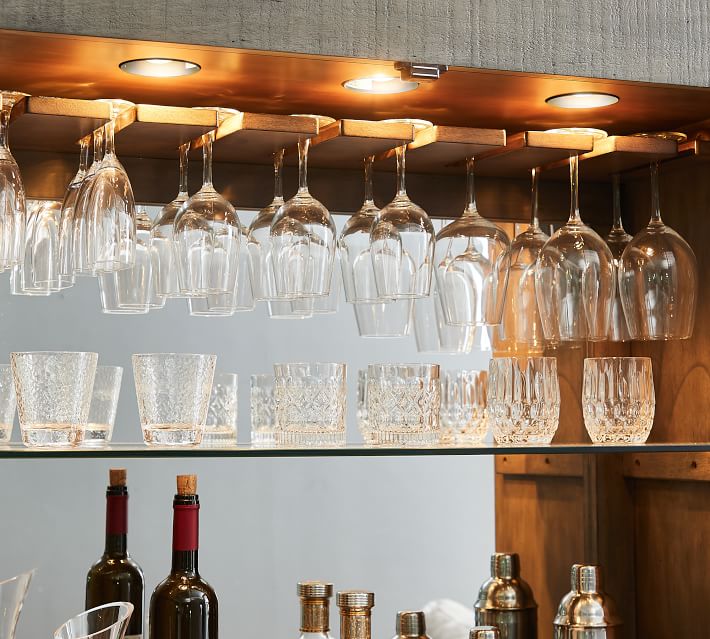 Under-cabinet lighting illuminating hanging wine glasses and a row of glassware and tumblers on shelves.