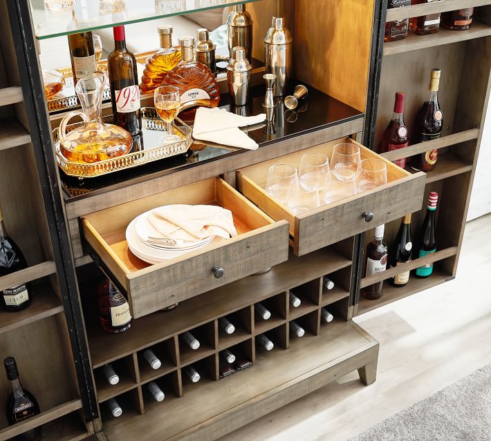 Home bar setup with liquor bottles, glasses, ice bucket, and pull-out drawers in a wooden cabinet.
