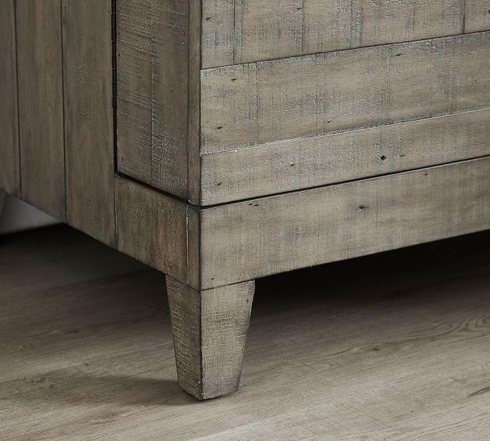 Close-up of the bottom corner of a rustic wooden cabinet with a tapered leg.