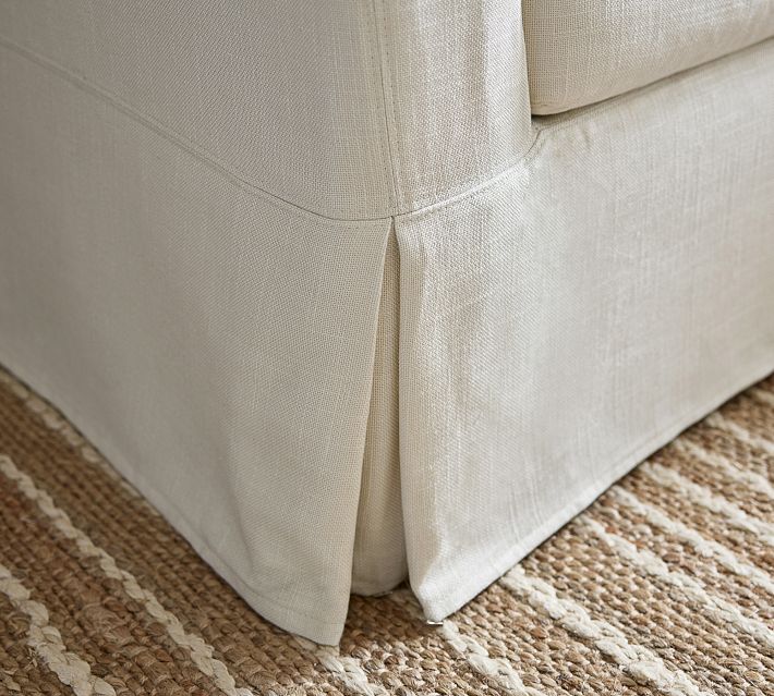 Corner of sofa with skirted plinth and pleated side panel on carpet.