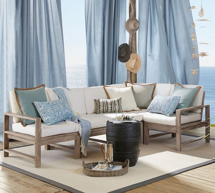Outdoor lounge sofa with blue and neutral cushions under blue curtains near the ocean