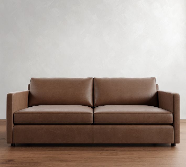 Large brown leather sofa with two seat cushions and back cushions against a light wall