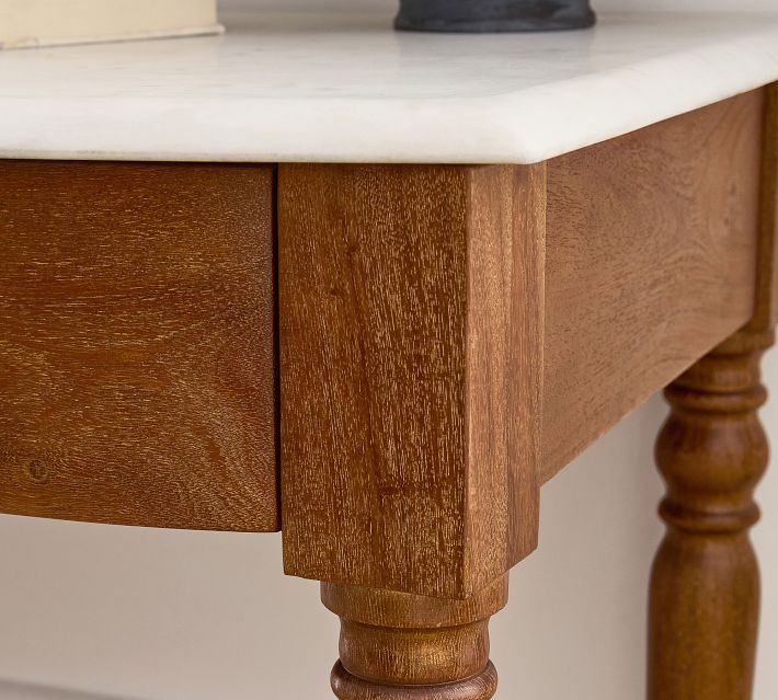 Corner of table with thick drawer front and turned leg, marble top edge.