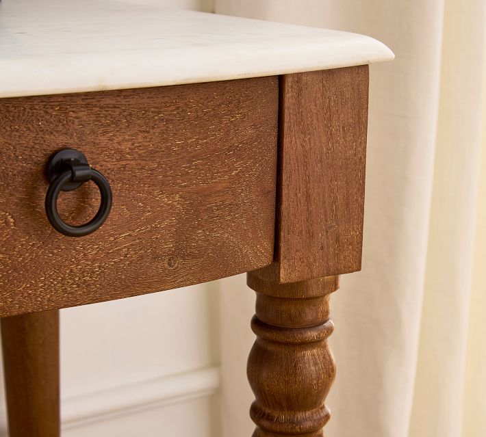 Close-up of a wooden drawer front with a round black ring pull and a turned leg.