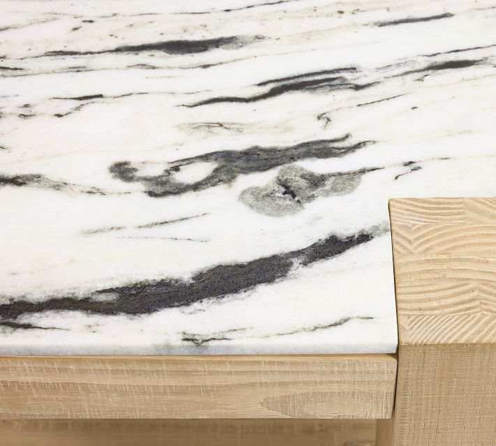 Close-up of a marble tabletop with gray veining resting on a light wood base.