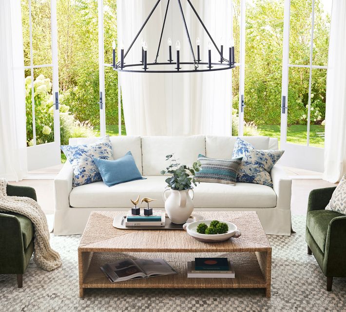Bright sunlit living room with white sofa and blue chairs, large windows.