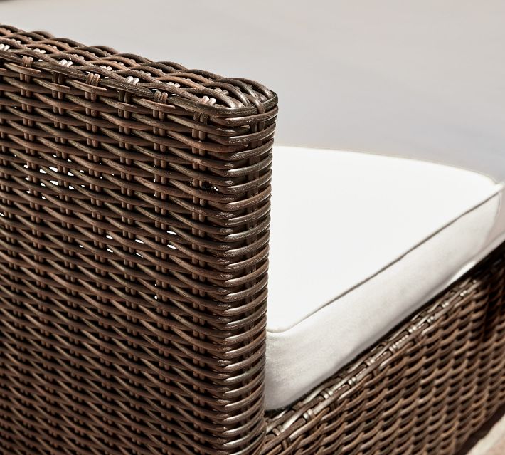 Close-up of brown wicker corner of outdoor sofa with white cushions