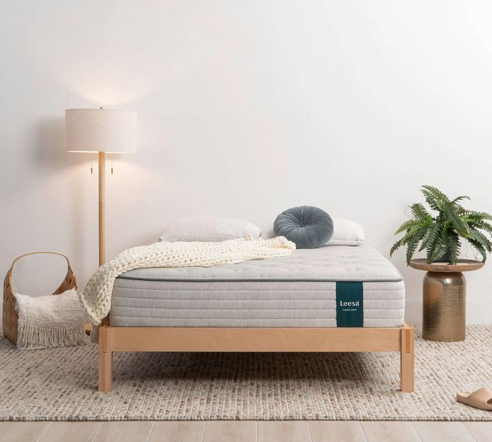 A minimal bedroom scene with a bed and a knitted blanket, pillow, and a plant, featuring a Leesa mattress.