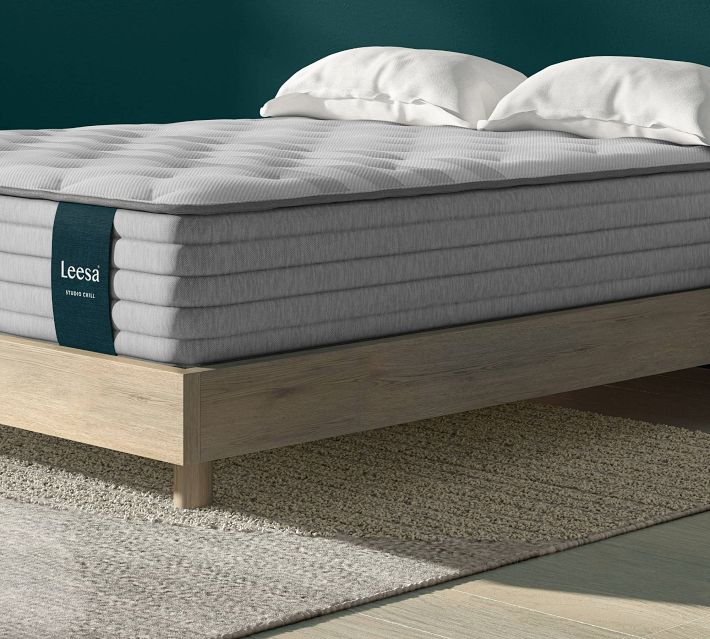Close-up of a plush light gray mattress with stitched lines and a dark teal Leesa label strapped around the side.