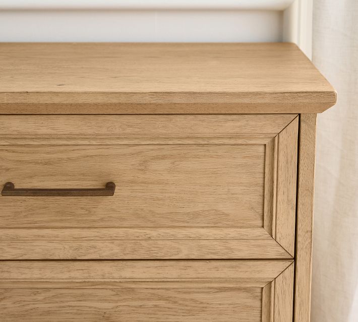 Close-up of a wooden dresser drawer front with a recessed panel and metal handle.