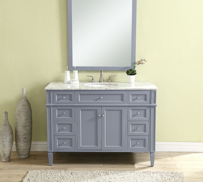 Grey-blue bathroom vanity with marble top and round mirror, in a bathroom with beige wall.