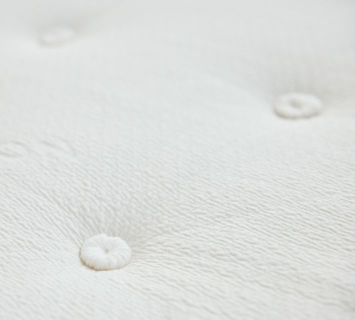 Close-up texture of a white mattress fabric with tufted buttons.