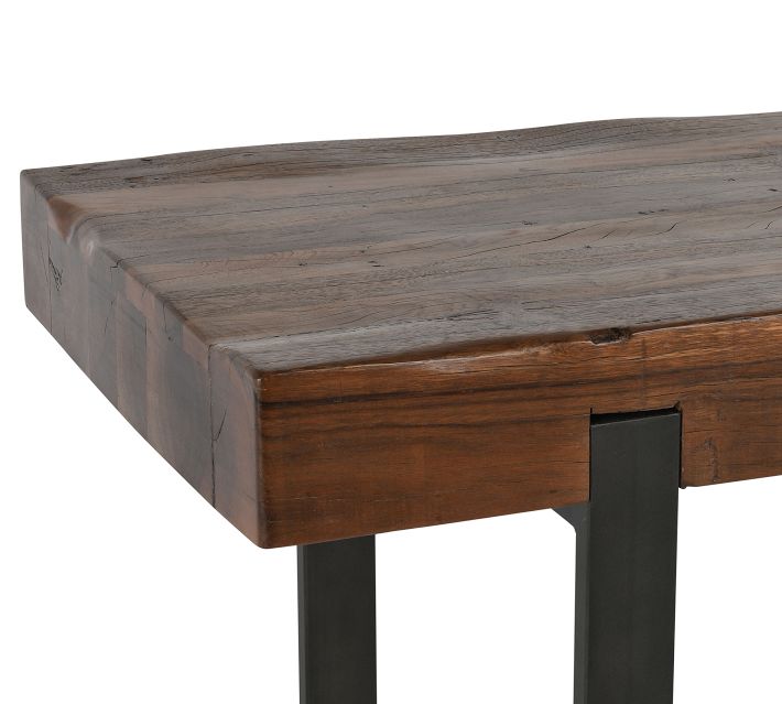 Close-up of the edge and corner of a wooden table top showing natural wood grain and a black metal leg