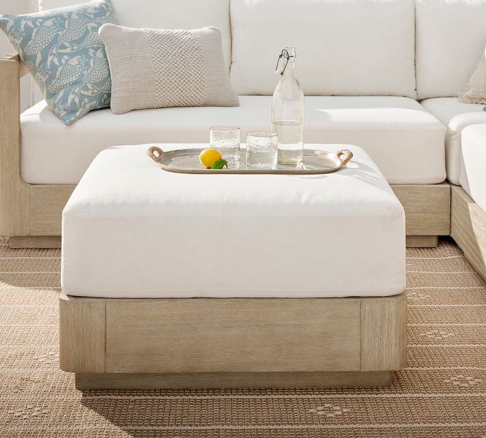 Outdoor sectional sofa with white cushions and wooden base, coffee table tray with bottle and lemon on beige woven rug