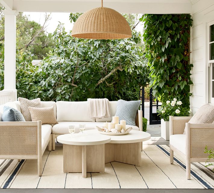 Close-up of large woven rattan pendant light hanging above outdoor seating, with greenery in background