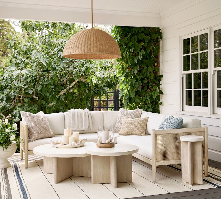 Outdoor sectional sofa with beige cushions and round nested coffee tables, woven cane panels, hanging wicker light