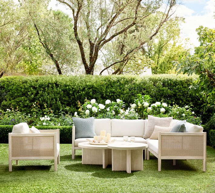 Outdoor living set with woven cane panels and light wood frame, cream cushions, arranged on lawn with greenery