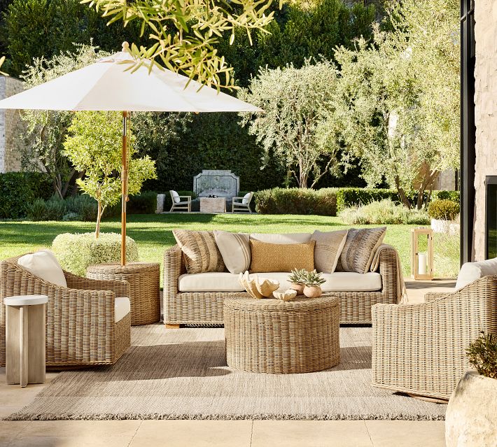 Patio seating area with wicker sofas, cushions, an umbrella, and a round coffee table set on a lawn.