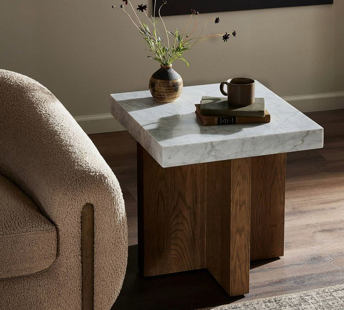 Side view of a modern two-toned end table with a white marble top and wooden base beside a beige textured chair
