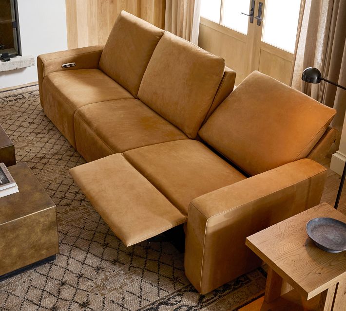 Open-forward reclining section of tan leather sofa showing leg support and chaise extension.