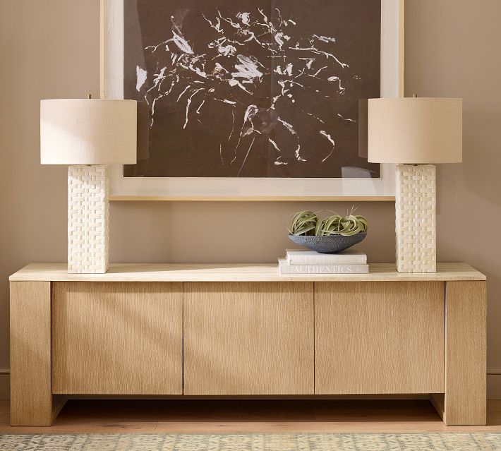 A wooden sideboard with two lamps and a framed artwork above, decorative bowl and books on top