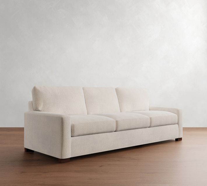 A light beige three-seat sofa shown in a three-quarter view, spacious with cushions.