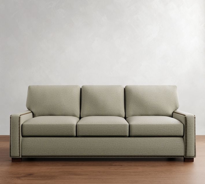 A light olive-green sofa with three back cushions and nailhead trim