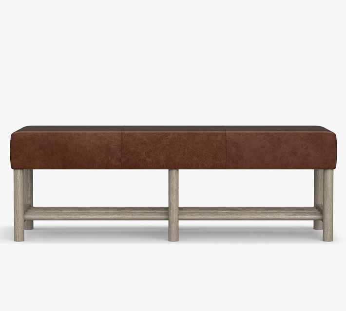 Wide shot of a brown leather bench with light wood-toned legs and a lower shelf.