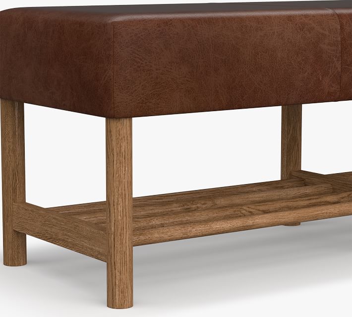 Close-up of the brown leather seat edge and wooden legs of the bench showing joints and texture.