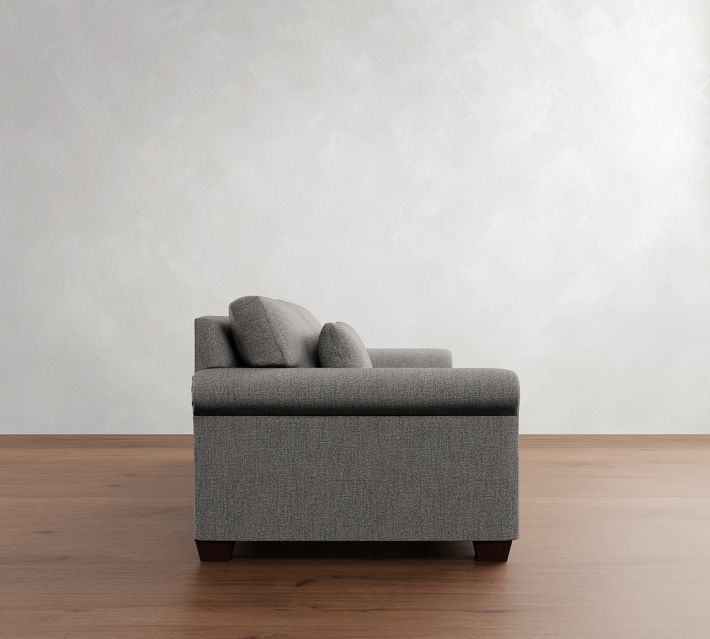 Side profile of a gray fabric sofa showing its depth, single elongated arm with cushions, and wooden legs.