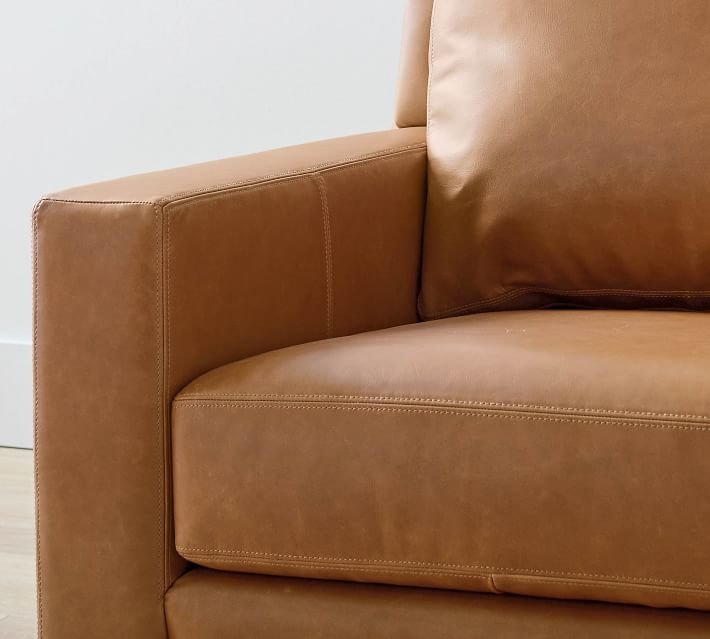 Armrest detail of brown leather sofa showing seam stitching and cushion