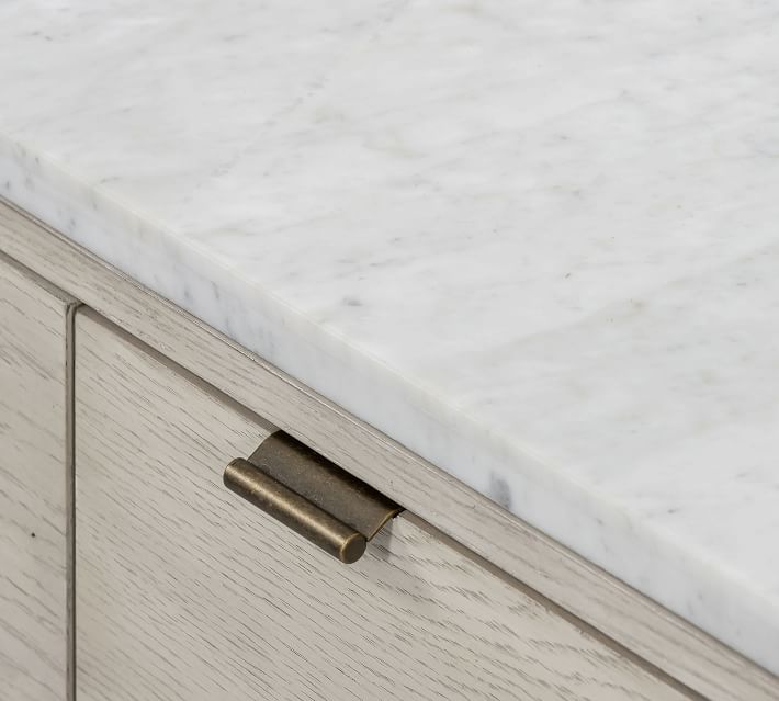 Close-up of a marble countertop edge overlaid on a wood drawer front with a brass handle