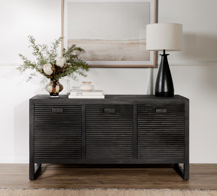 Dark wood sideboard with three cabinet doors, decorative vase and lamp on top
