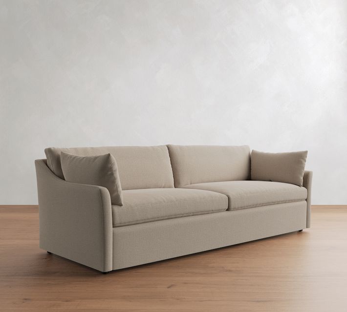 Beige fabric sofa with three seat cushions and three back cushions, armrests at ends, on wooden floor.
