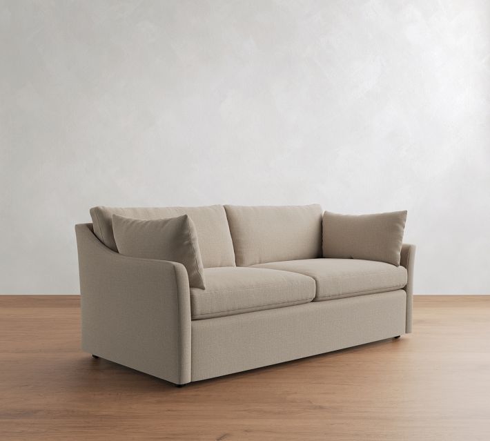 Three-quarter view of beige sofa with cushions, showing left armrest and three cushions.