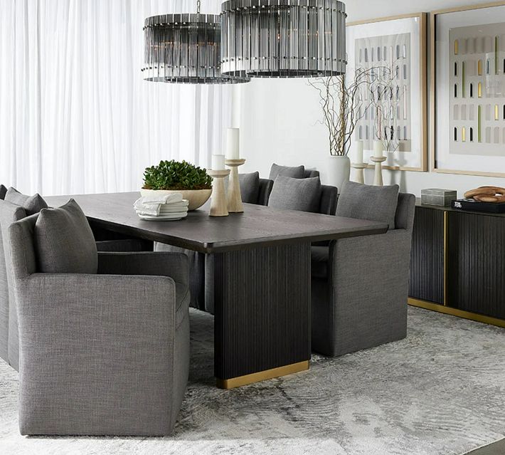 Dining room scene with a large dark wood table, ribbed legs, gray upholstered chairs, and decorative elements.