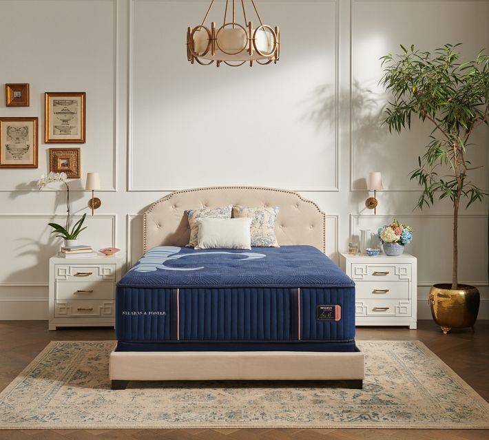 Elegant master bedroom with navy blue mattress and upholstered headboard, framed wall panels, nightstands, and decor.