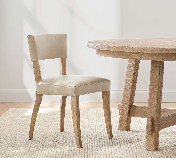 Beige upholstered chair with wooden legs placed beside a round wooden table